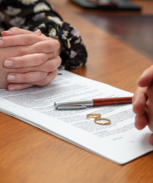 Signing a divorce, marriage dissolution documents and agreement. Wife and husband hands, wedding rings and legal papers for signature on a wooden table, lawyer office