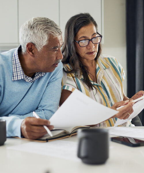 An older couple is sitting at their kitchen table reviewing financial documents.