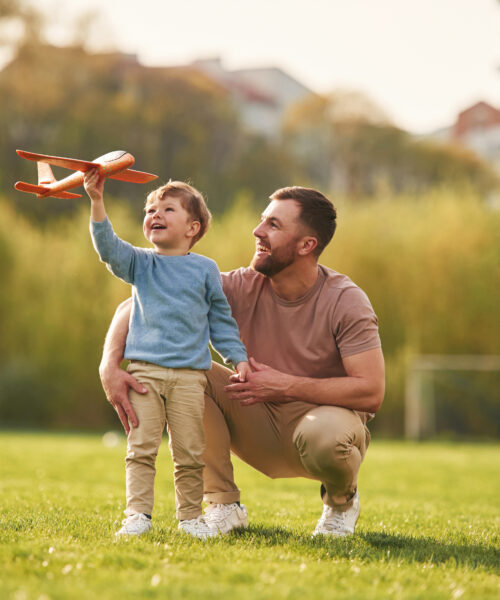 Weekend activities. Playing with toy plane. Happy father with son are having fun on the field at summertime.