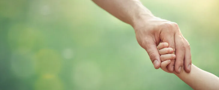Fathers hand holding his little child in sunny day outdoor, united family and happy childhood concept, banner format with copy space.